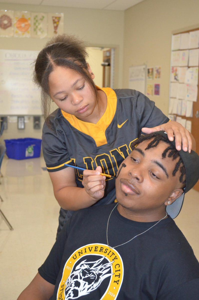 Makayla Stewart, senior, paints a gold and black U symbol onto U-Times Web Editor Xavier Thomas face before the Homecoming pep rally Sept. 29.