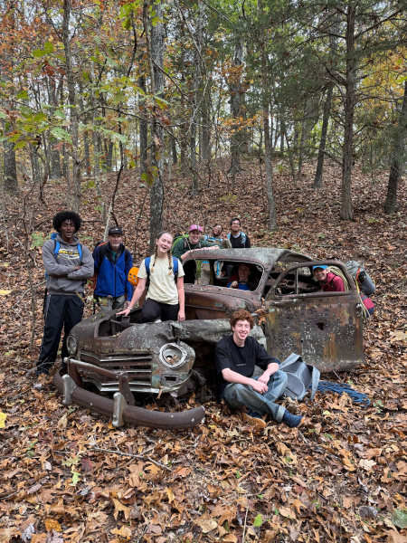 A group of Eco-Actors pose around a rusty old car in the forest near Green's Cave.